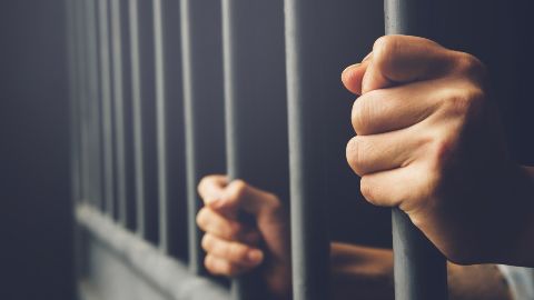 Hands on the bars of a jail cell
