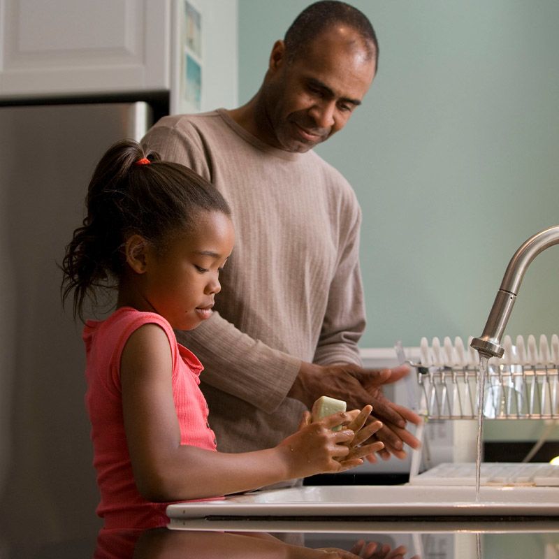 Older man helping a kid wash her hands at a kitchen sink