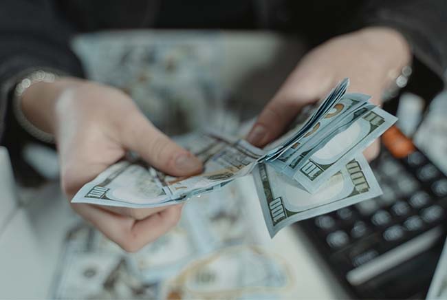 Woman holding cash and counting money with a calculator sitting on the table