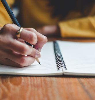 Woman writing on a notebook with a pencil while wearing a gold ring