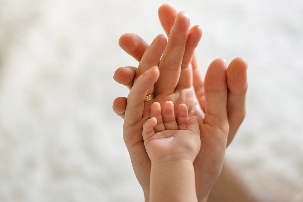 adult hands holding an infant hand
