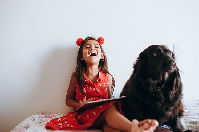 Girl playing with a book and a dog sitting next to her